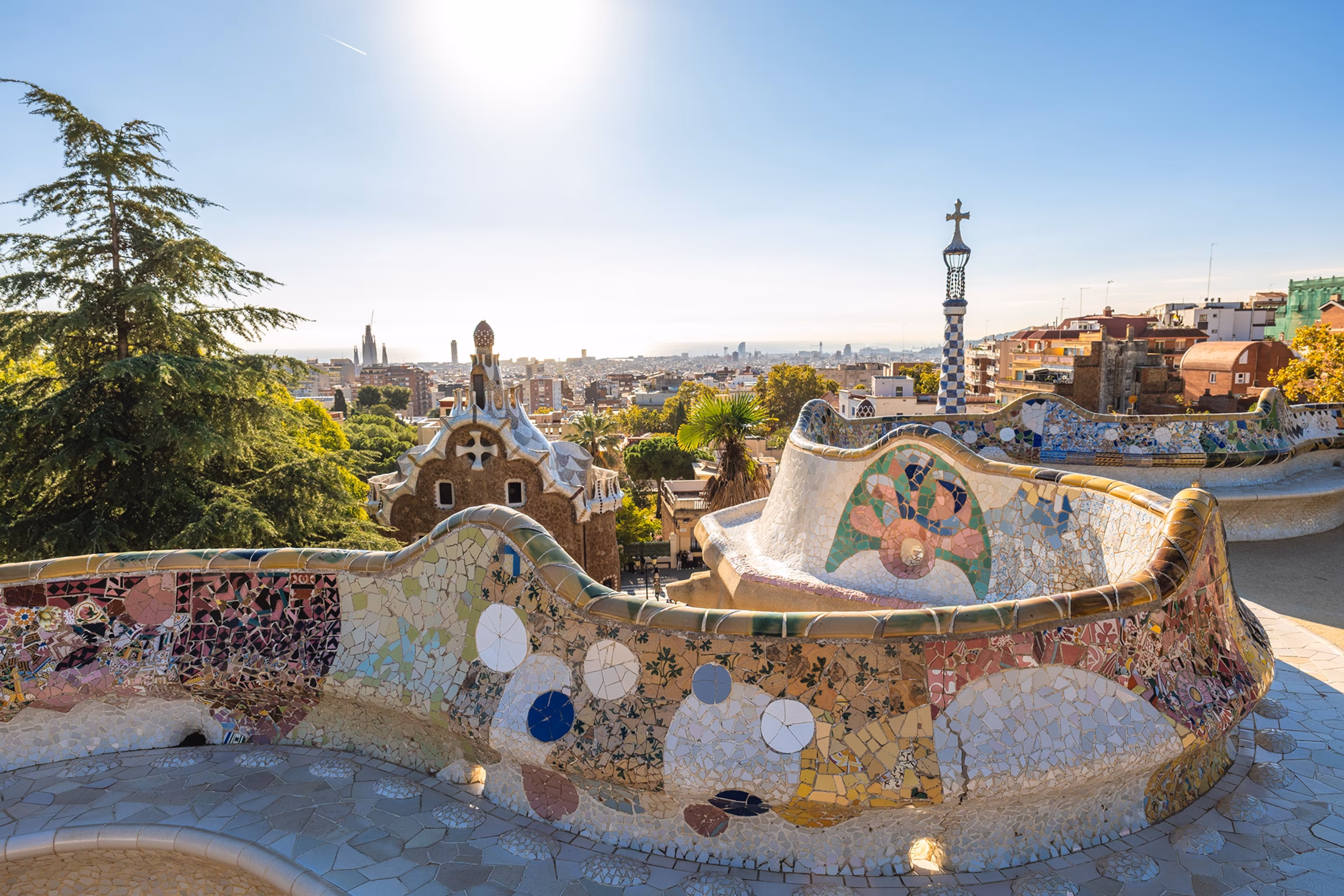 En buet bænk dekoreret med fliser i et mosaikmønster har udsigt over byen Barcelona.