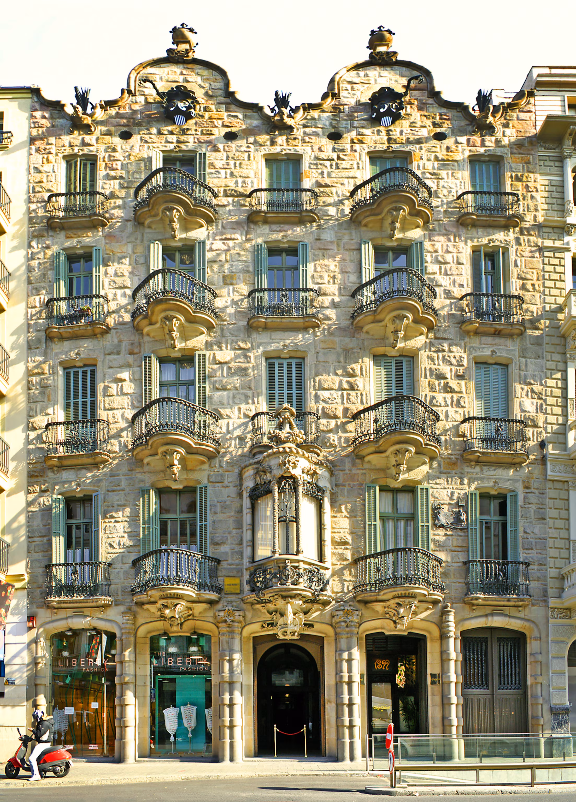 Facade på bygning med smedejernsbalkoner og mange vinduer, designet af Gaudi.