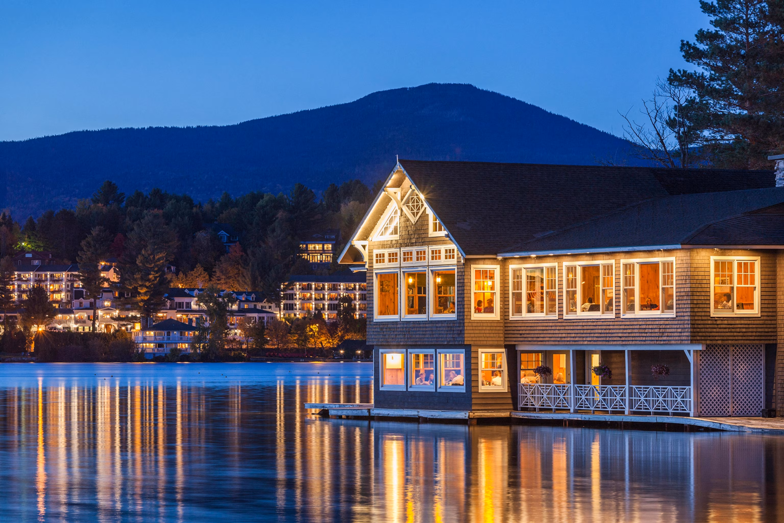 En natlig udsigt over en restaurant ved søen, der lyser af lys, reflekteret i vand