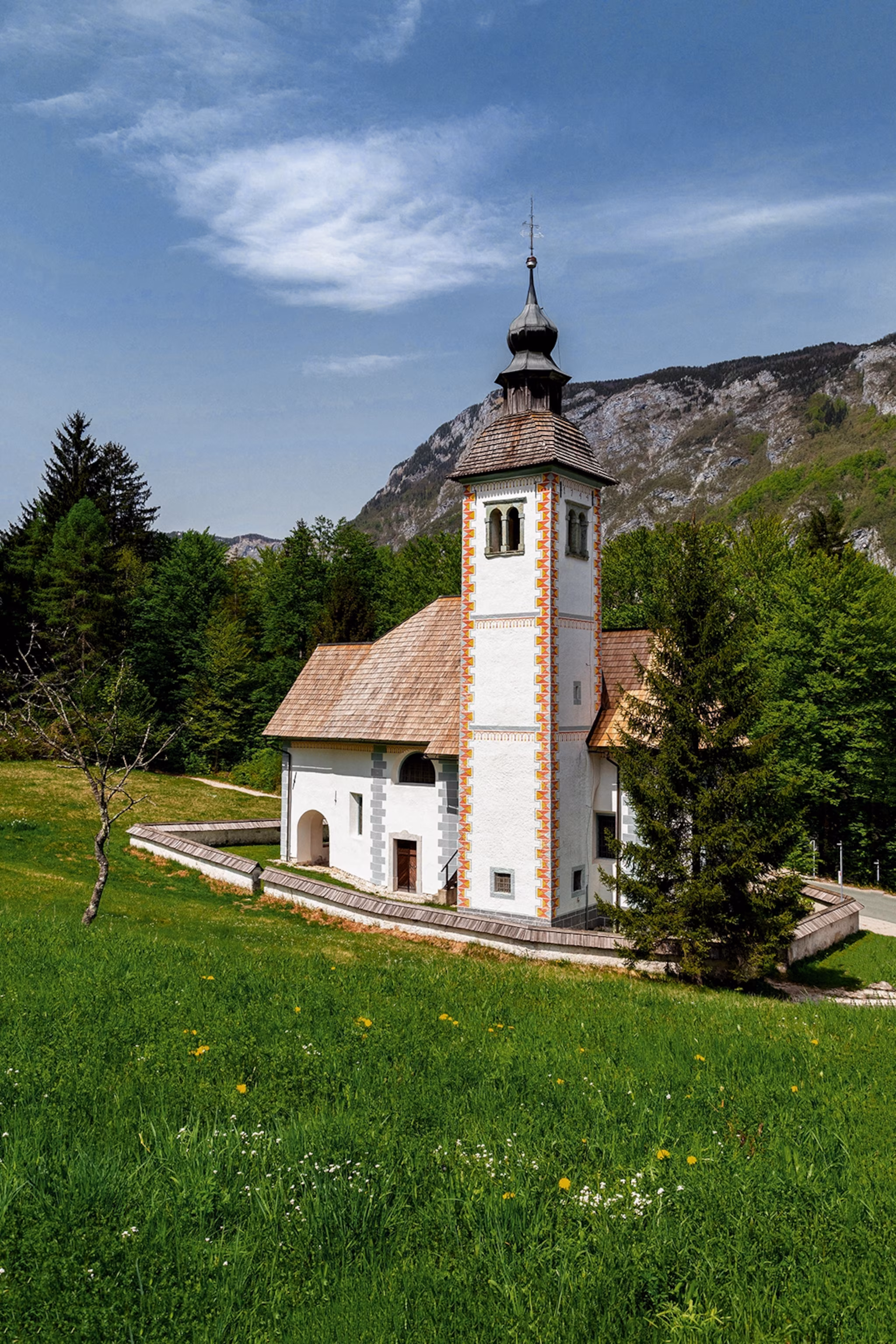 En lille kirke på græsskråningen af ​​en bakke med træer i ryggen.