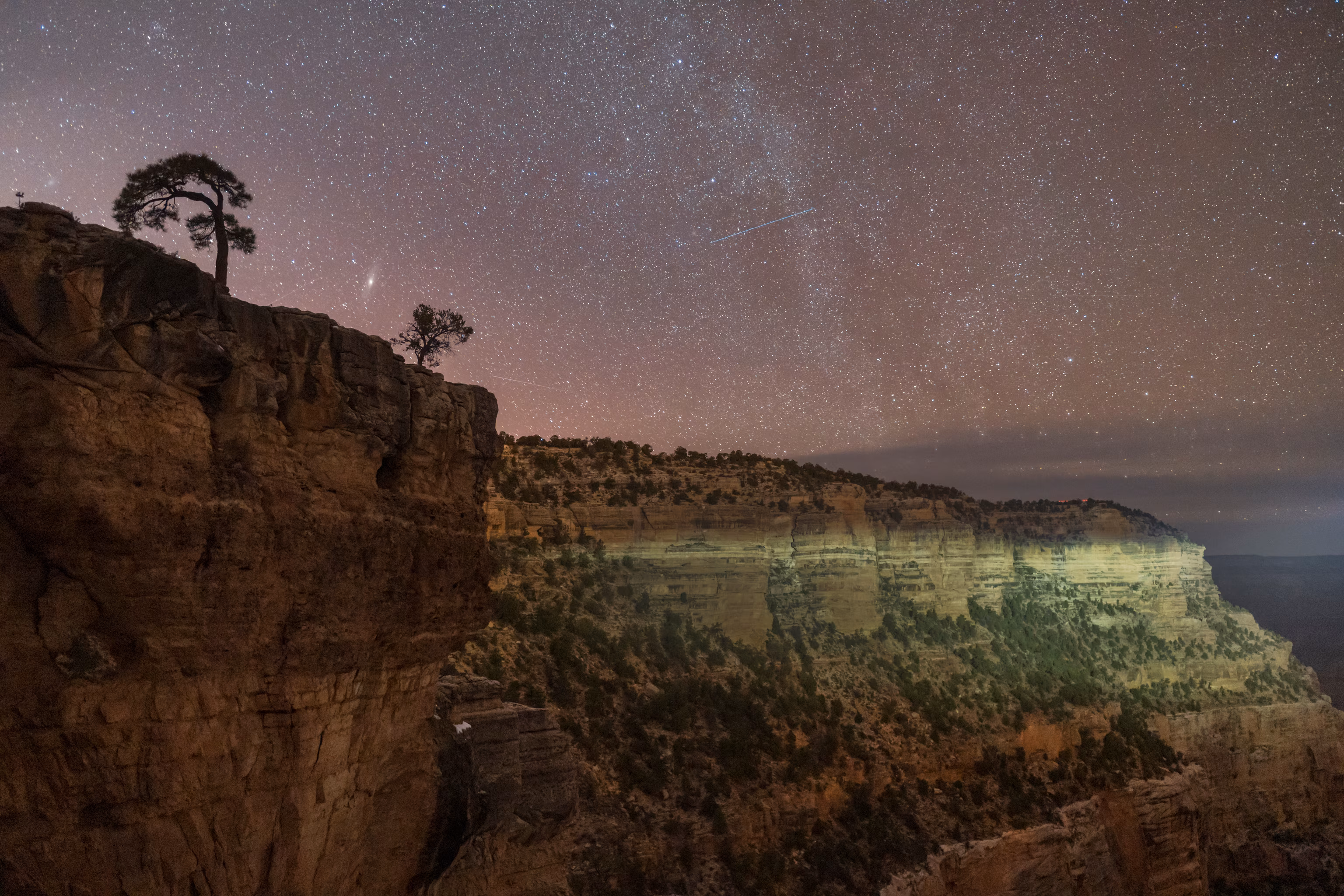 En side af Grand Canyon er oplyst af en forbipasserende bils forlygte, med nattehimlen bagved fuld af stjerner