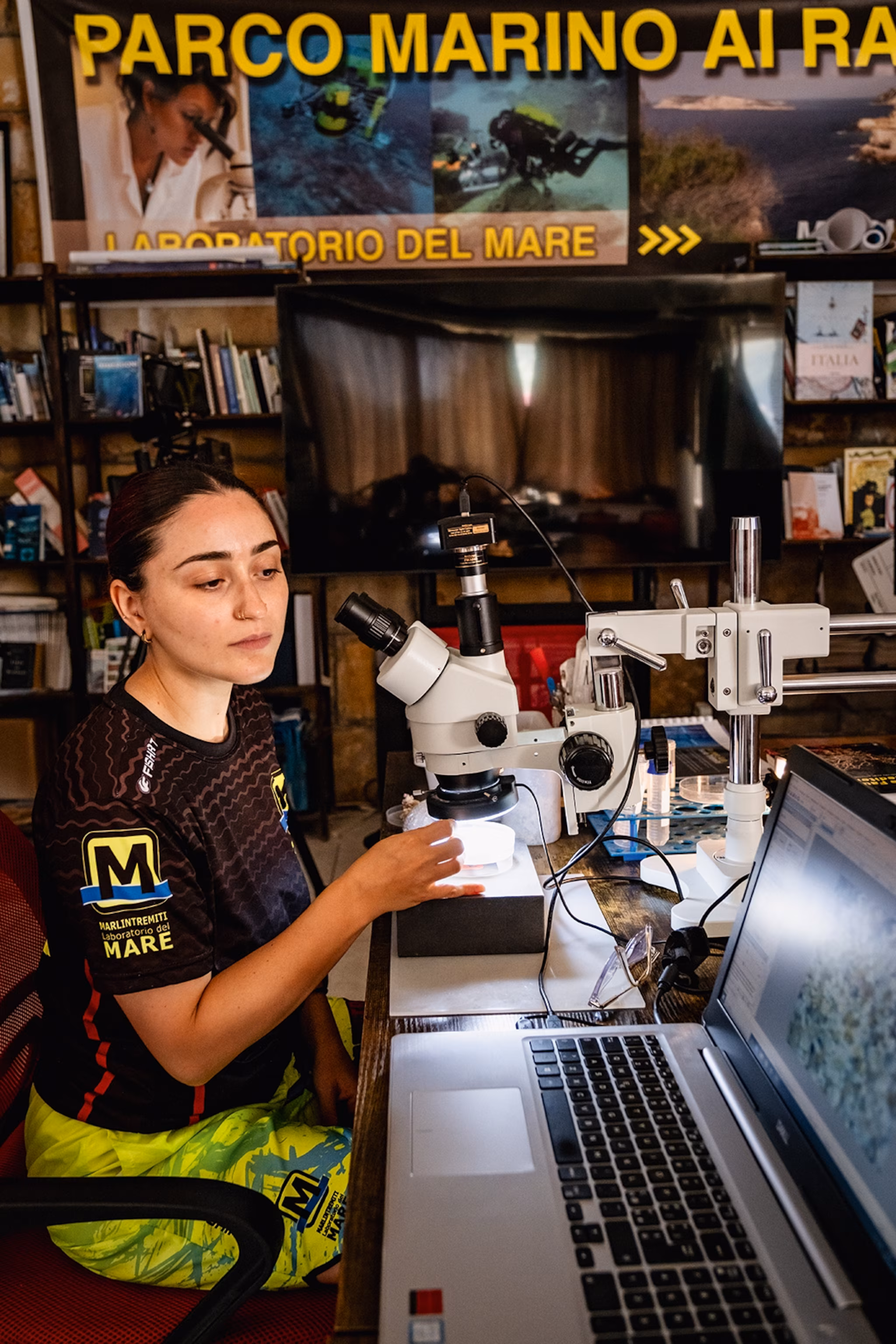 En ung kvindelig marinebiolog undersøger en sonde under et mikroskop i et laboratorium.