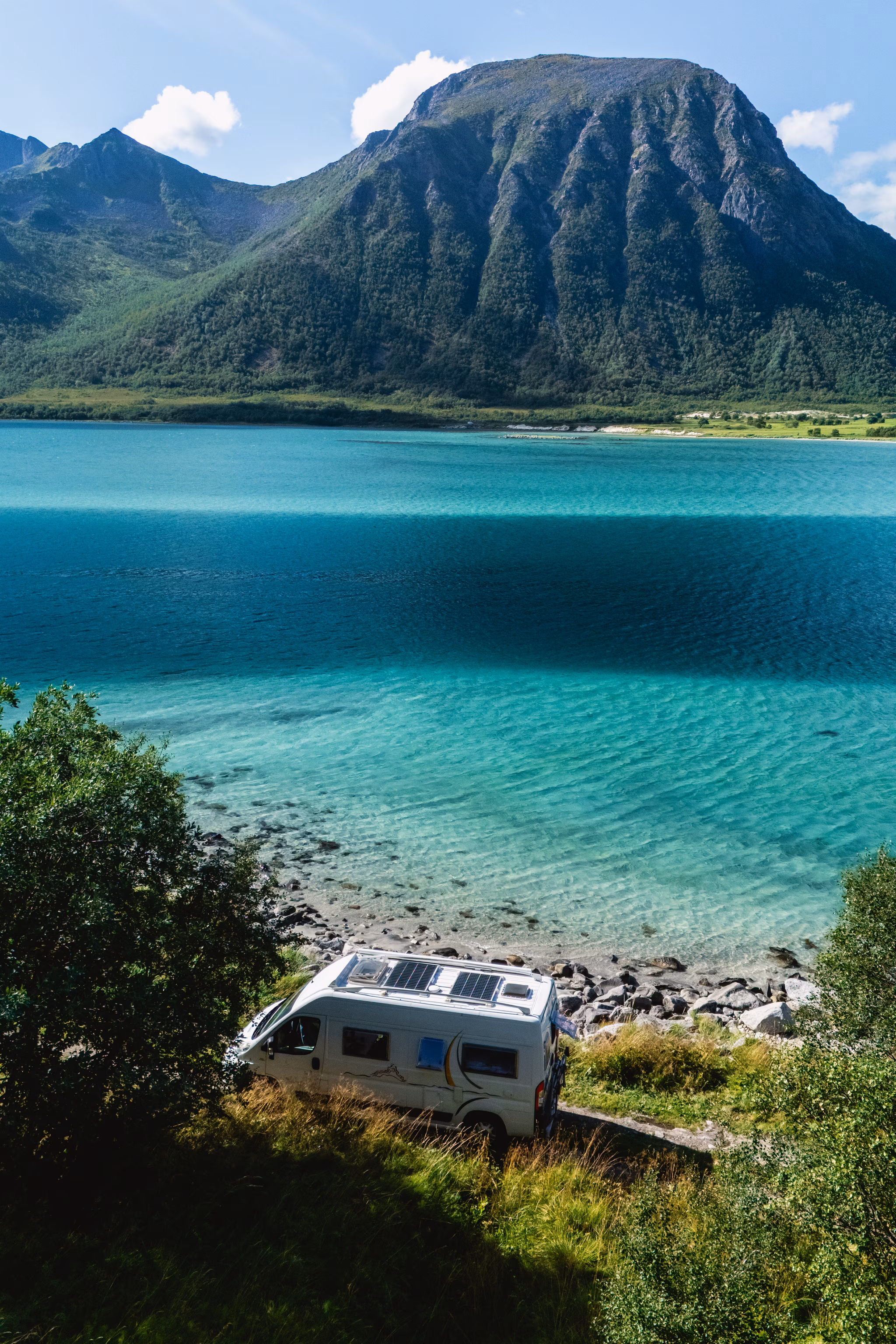 Campingvogn ved blåt vand og bjergskyline