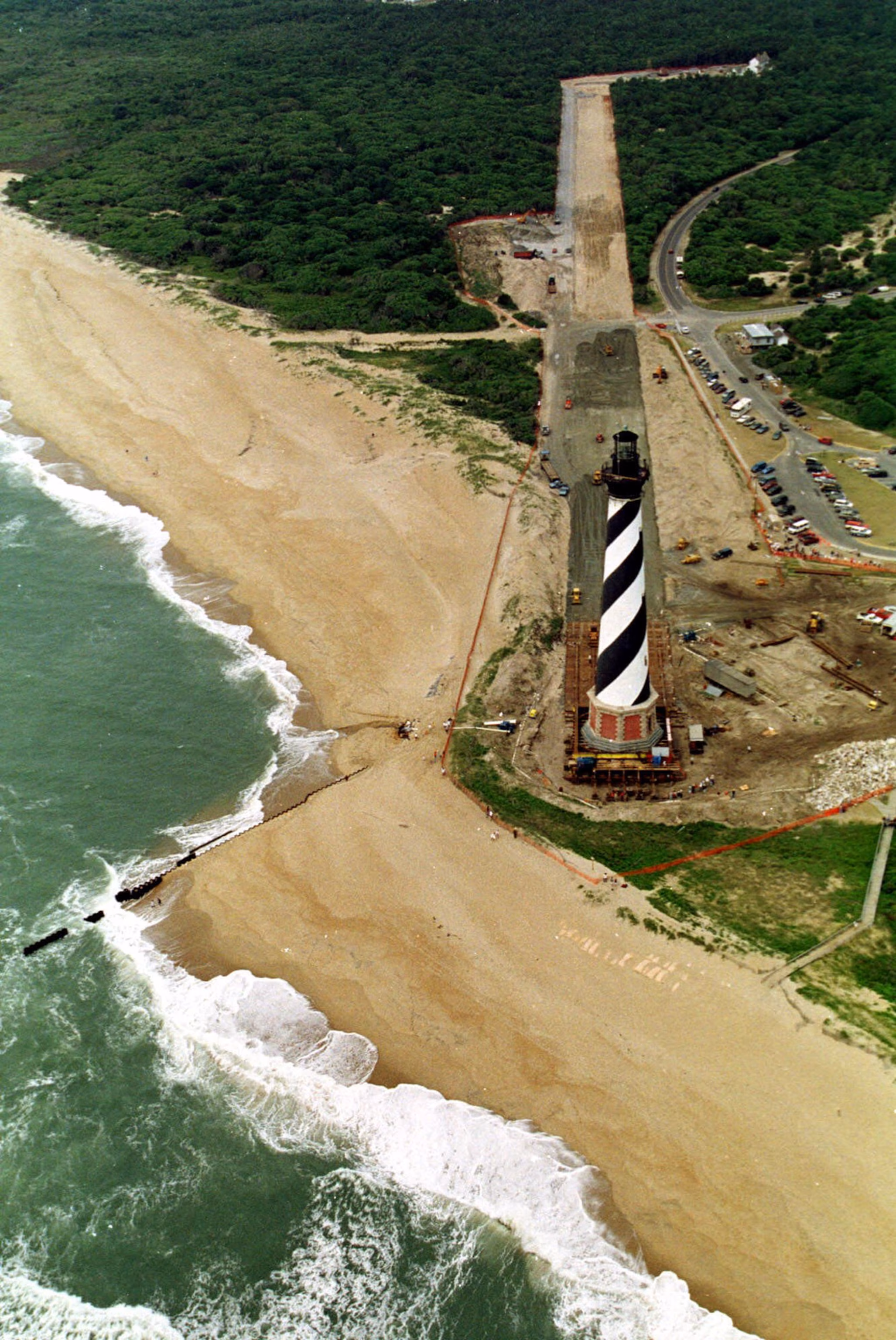 Bølger slår ned langs stranden, mens ingeniører fortsætter med at flytte Cape Hatteras Lighthouse i Buxton NC, fredag ​​den 18. juni 1999. Arbejdere skynder sig at flytte fyrtårnet 1.800 af de i alt 2.900 fod af flytningen for at beskytte det mod stranderosion. Når det er færdigt, vil fyret blive sat på en ny base øverst på billedet.