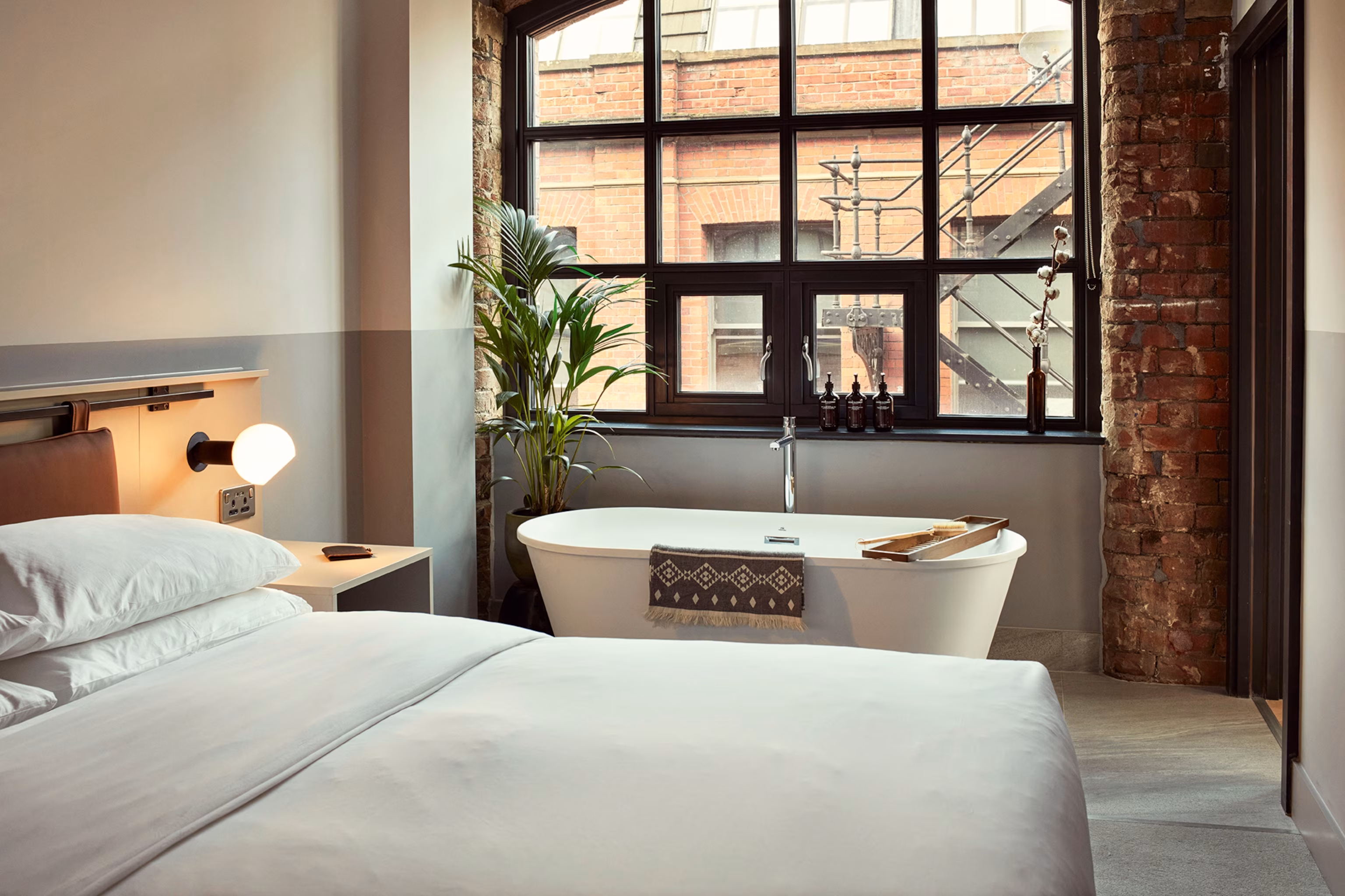 Et hotelsoveværelse i industriel stil med et fritstående badekar.