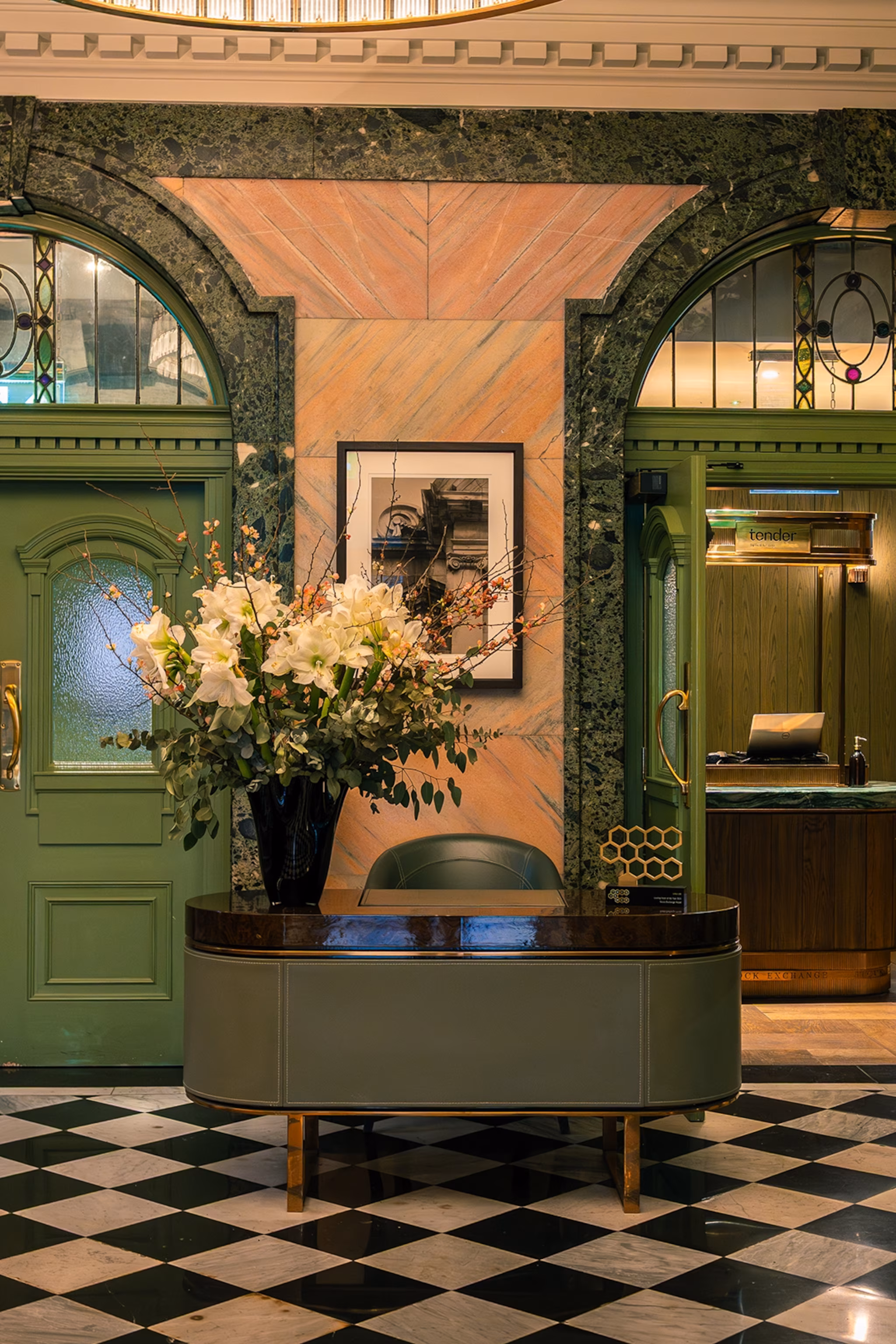 En luksuriøs hotellobby med malede, buede døre, et marmorflisegulv og en stor buket i receptionen.
