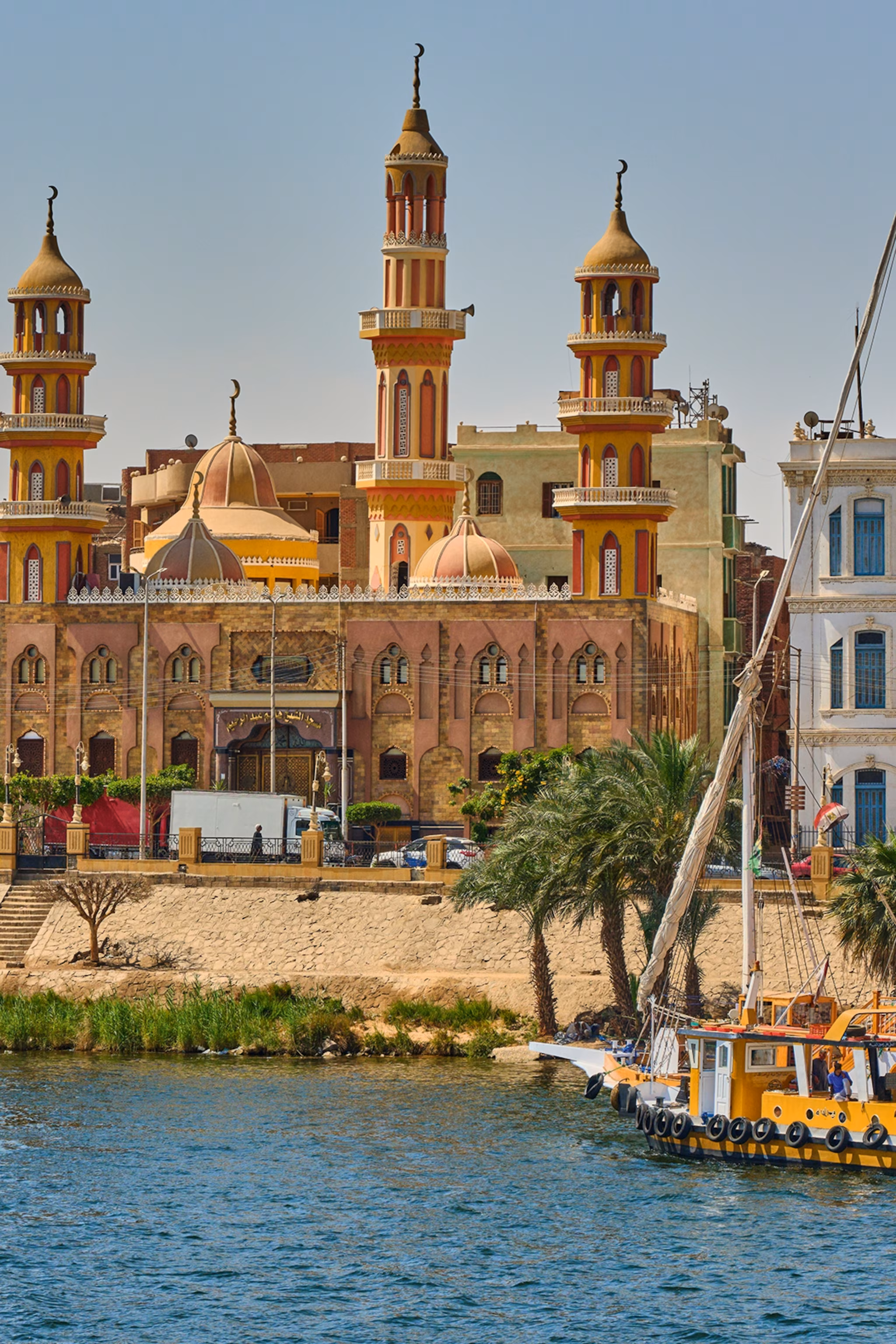 En flodfront i Egypten med farverige og romantiske bygninger samt traditionelle træbåde forankret på kysten.