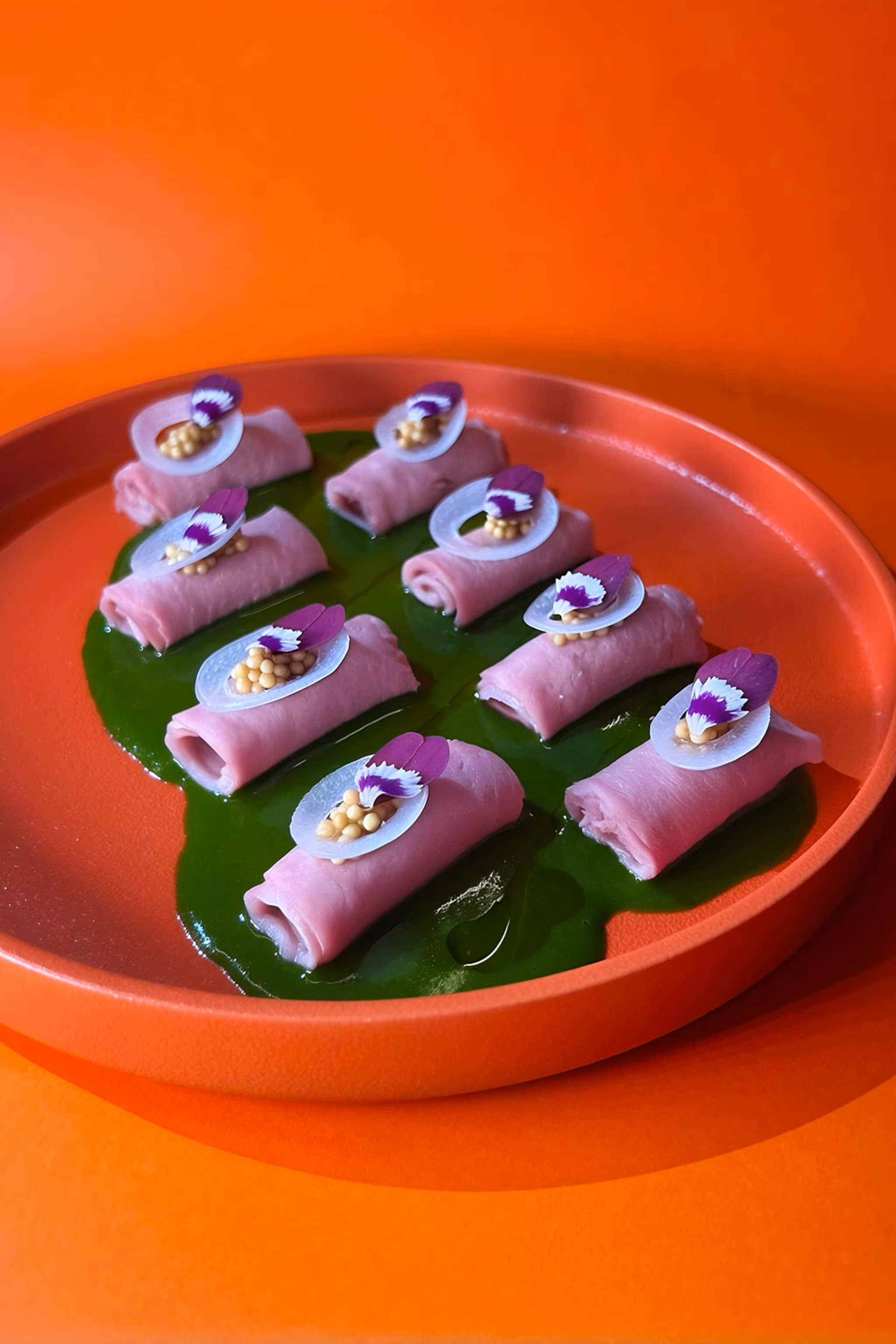Et nærbillede af et fad med små ruller andekød med en lilla sauce over toppen.