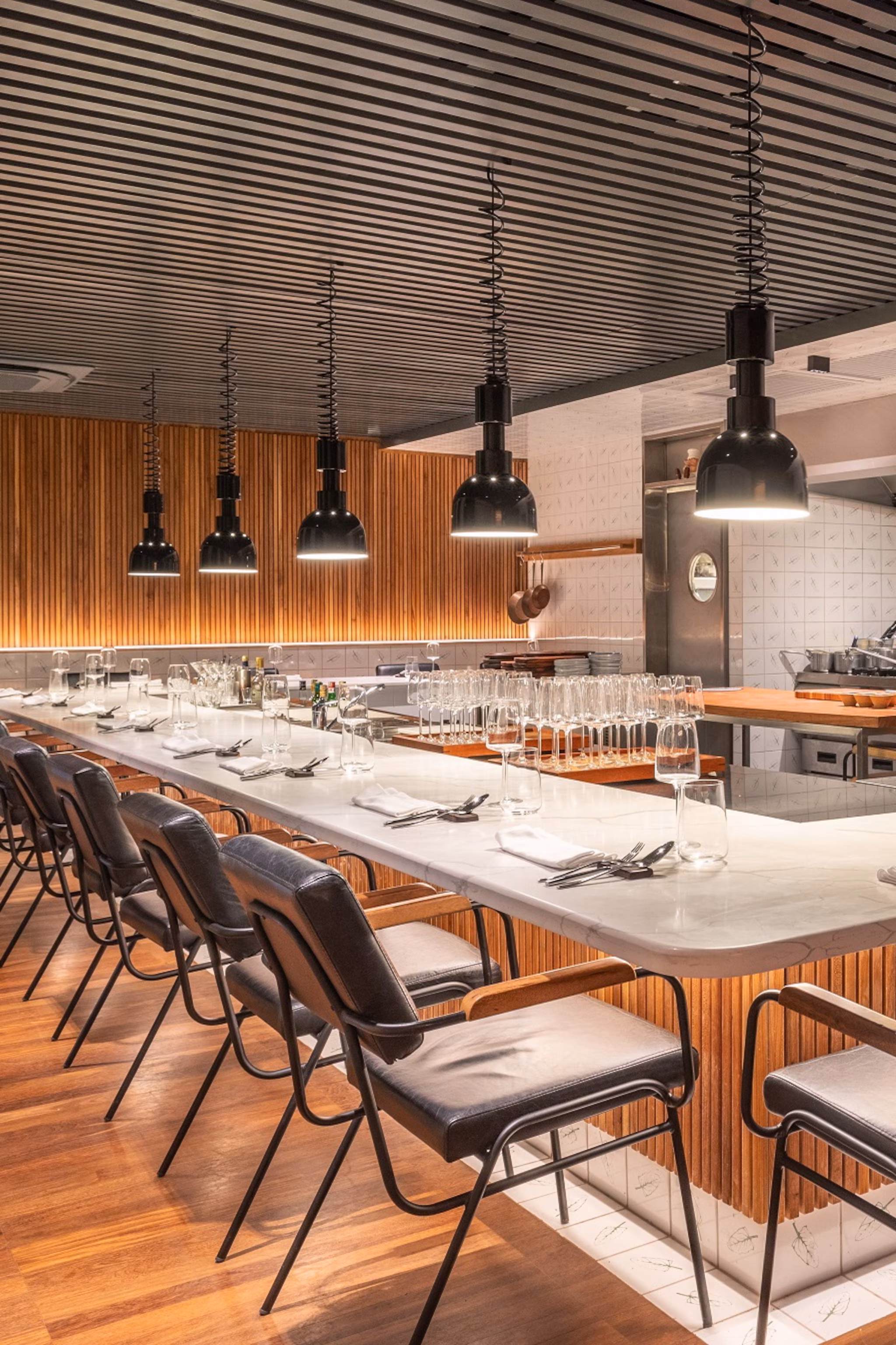 Interiøret af en moderne restaurant med bar siddepladser omkring et køkken.