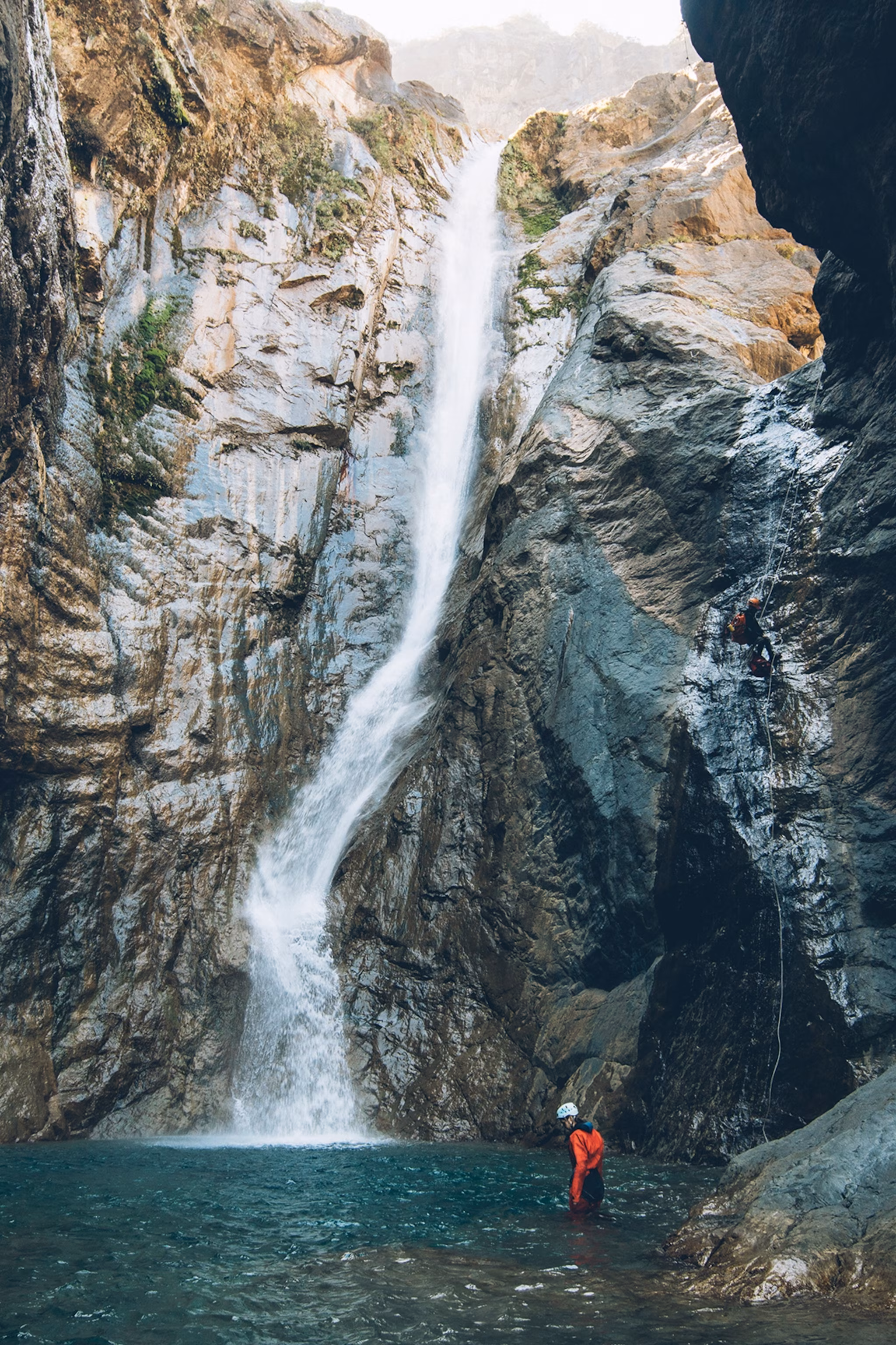 En dramatisk åben hule med et vandfald, der styrter ned i en naturlig pool nedenfor.