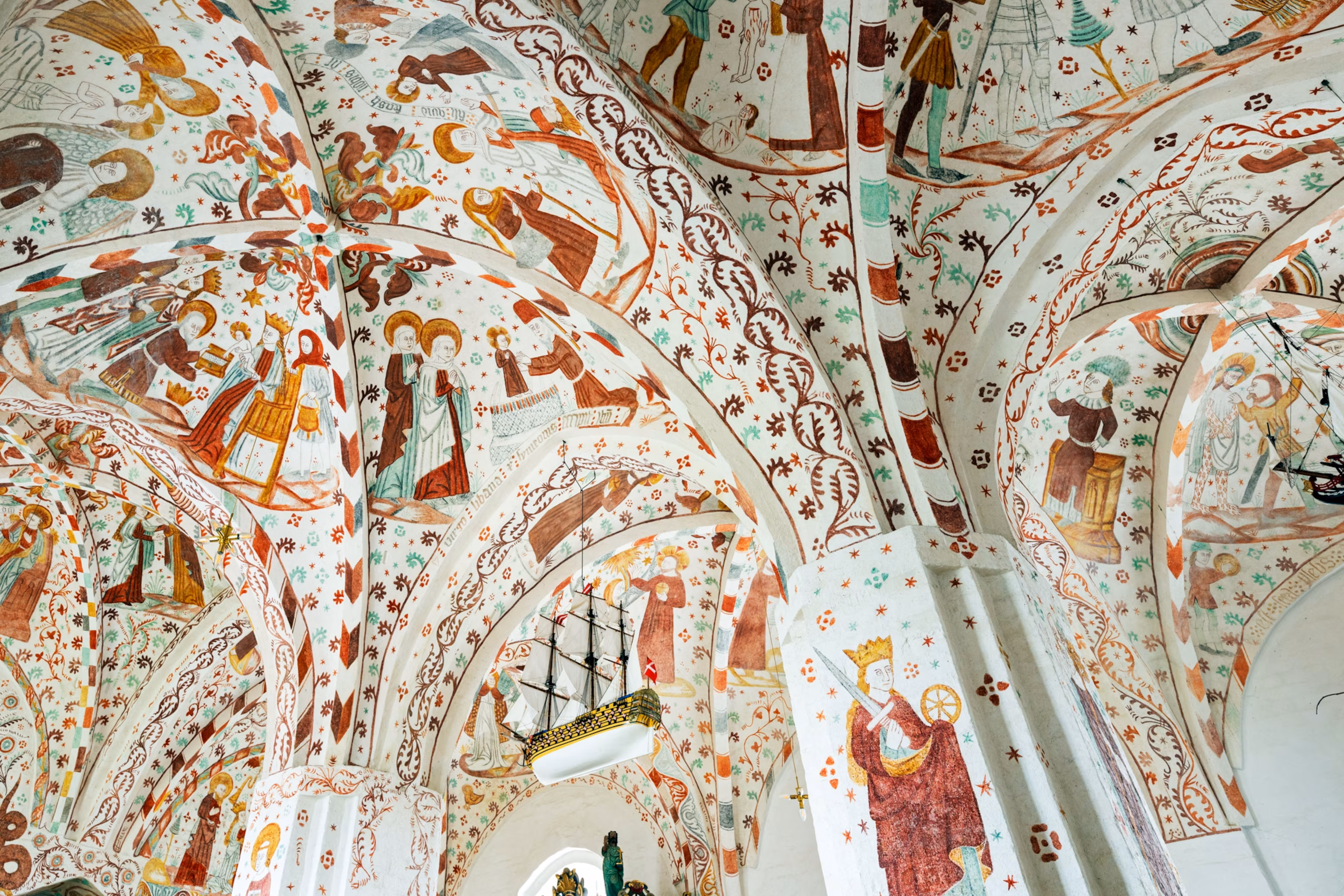 Det hvælvede loft i Fanefjord Kirke på Møn er dækket af en ekstraordinær samling af middelalderfresker, der skildrer bibelske historier, religiøse figurer og scener fra hverdagen.