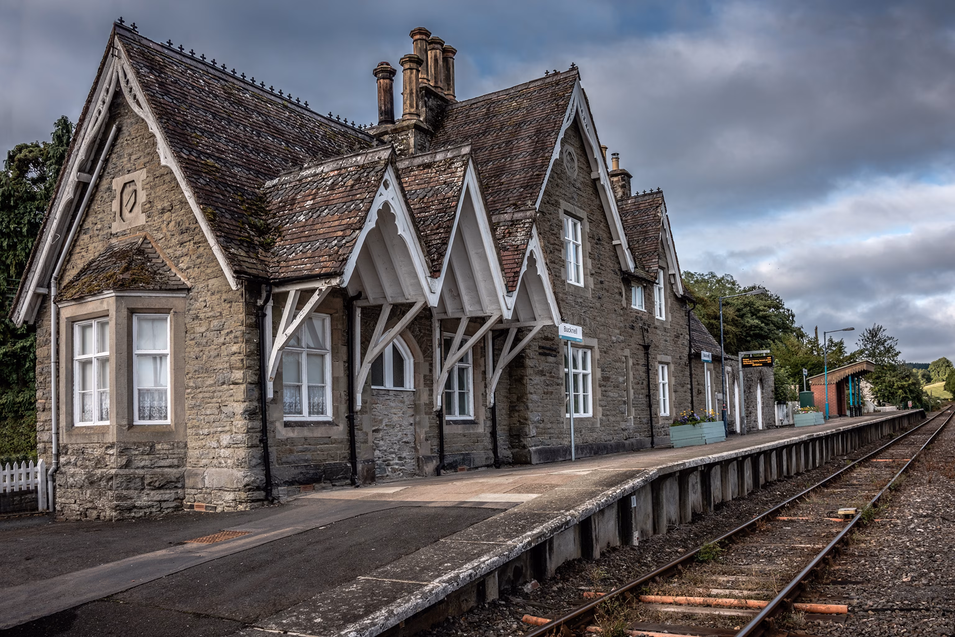 Murstensstationsbygning ved siden af en kort perron med jernbaneskinner og en overskyet himmel